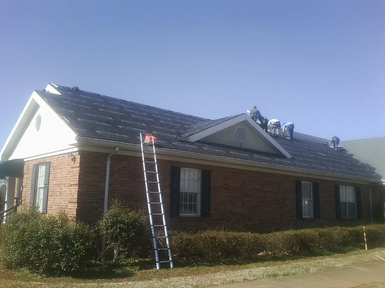 Crew tearing shingles off a brick ranch roof with a ladder set — Emergency Roof Repair work by our crew in Warrior
