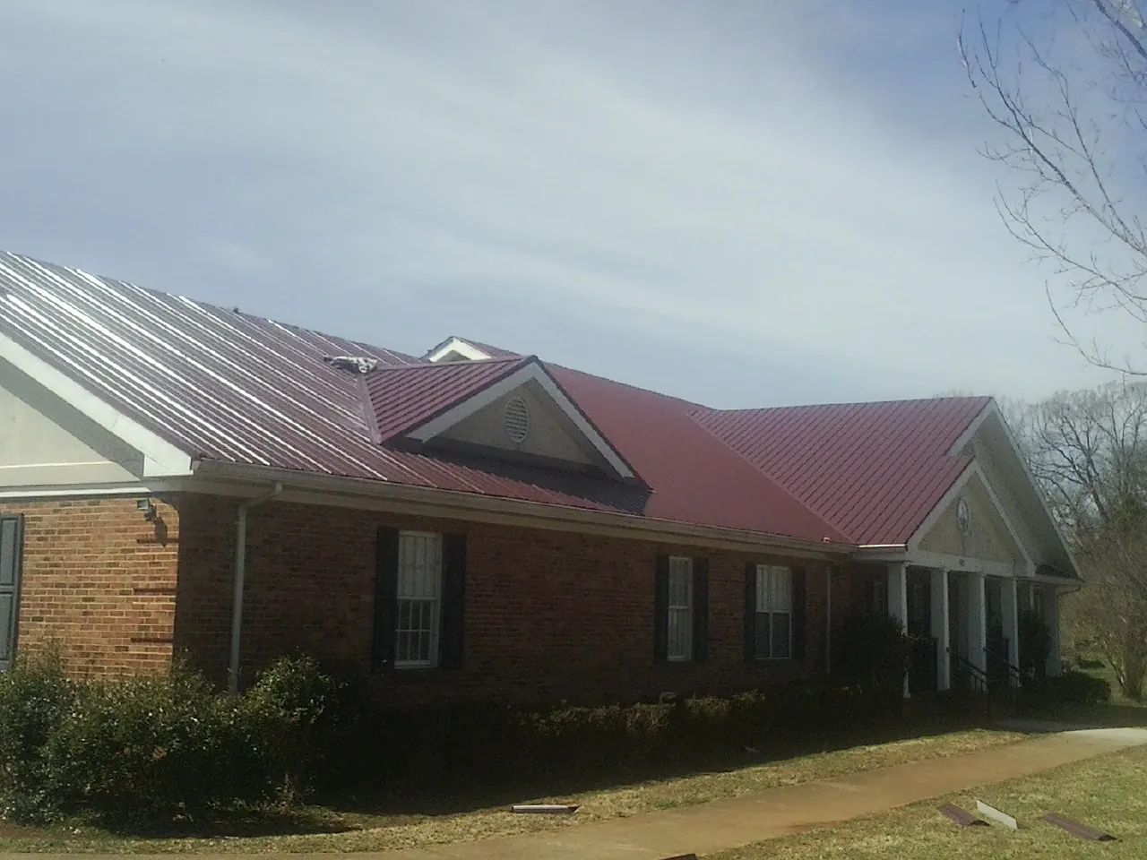 Red metal roof with gabled entries on a long brick building, from a Hail Damage Roof Repair job in Warrior