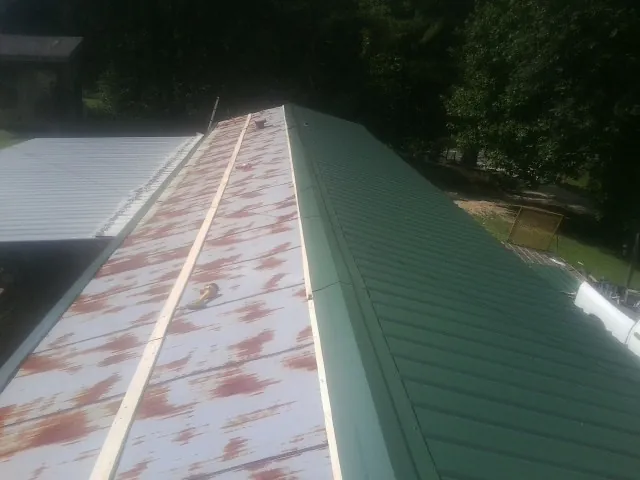 Old rusted panels beside newly installed green metal roofing — Wind Damage Roof Repair by Roofing Brothers in Warrior