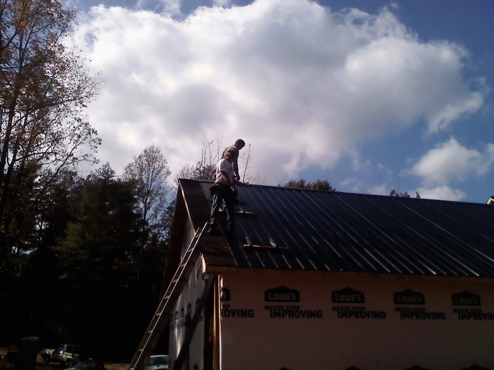 Roofer fastening dark metal panels high against a cloudy sky, from a Roof Inspection job in Warrior