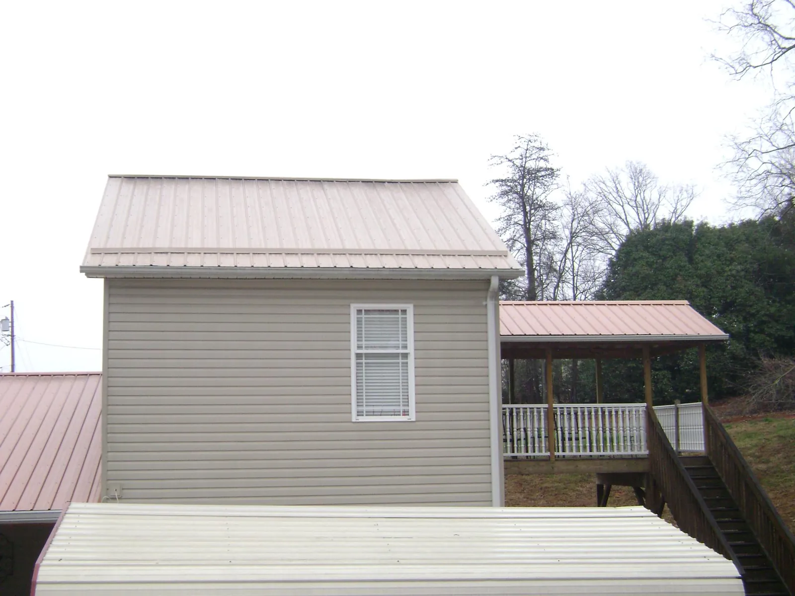 Tan metal roofs on a two story addition and attached porch, from a Roof Replacement job in Warrior