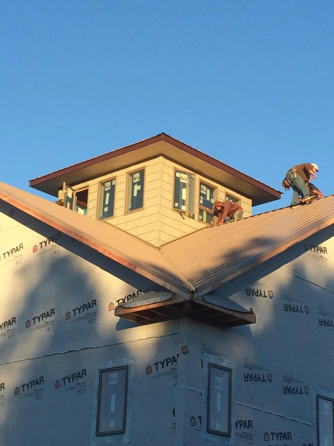 Roofers working around a rooftop cupola on a new metal roof at sunset — Roof Waterproofing in Warrior by Roofing Brothers